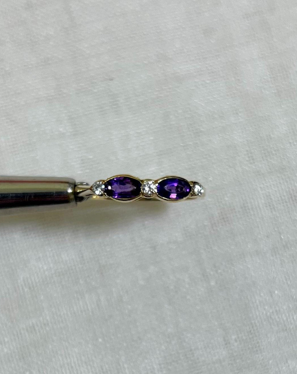 Gold ring with purple amethyst stone and diamond accents held by silver tool above light beige background