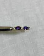 Gold ring with purple amethyst stone and diamond accents held by silver tool above light beige background