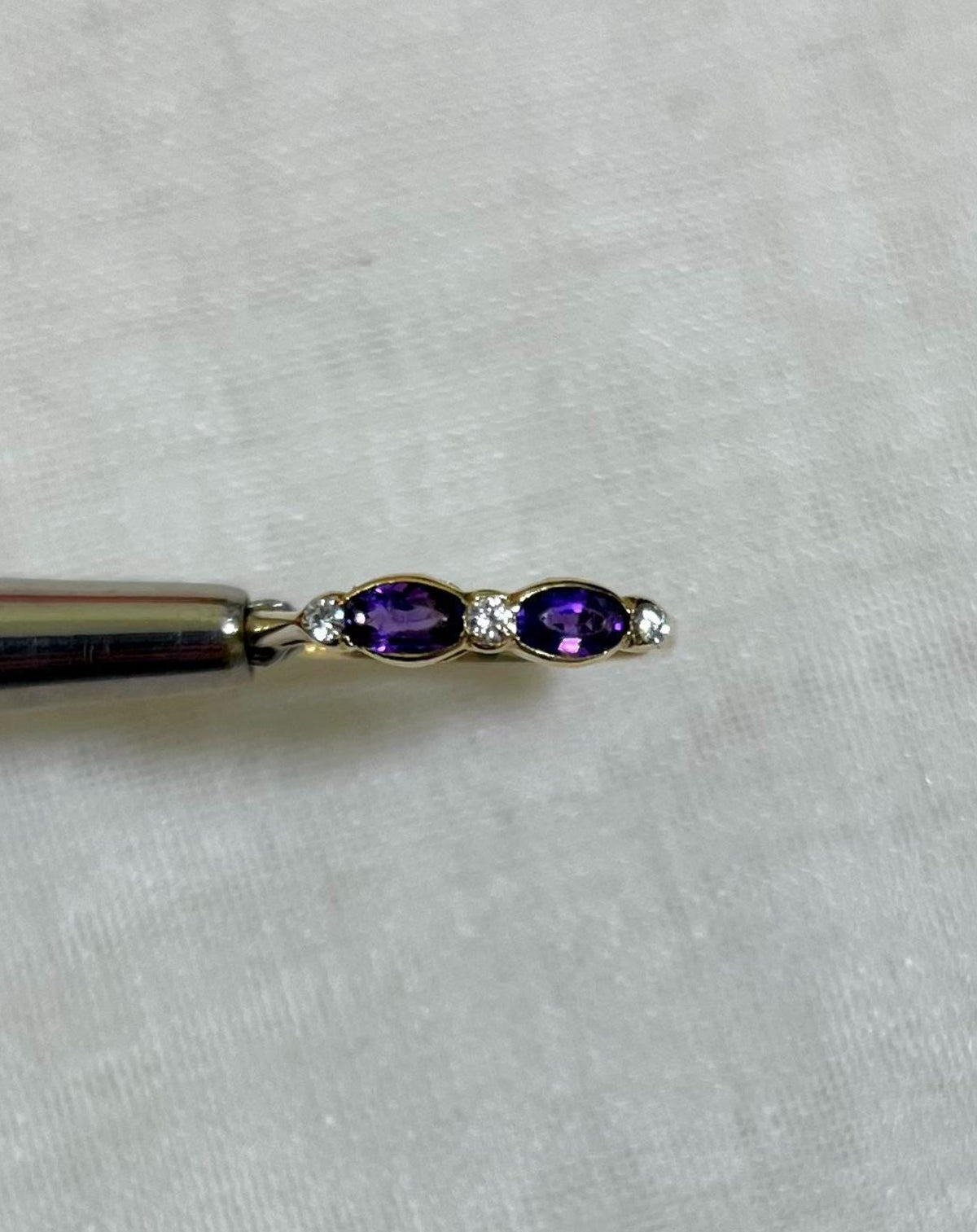 Gold ring with purple amethyst stone and diamond accents held by silver tool above light beige background
