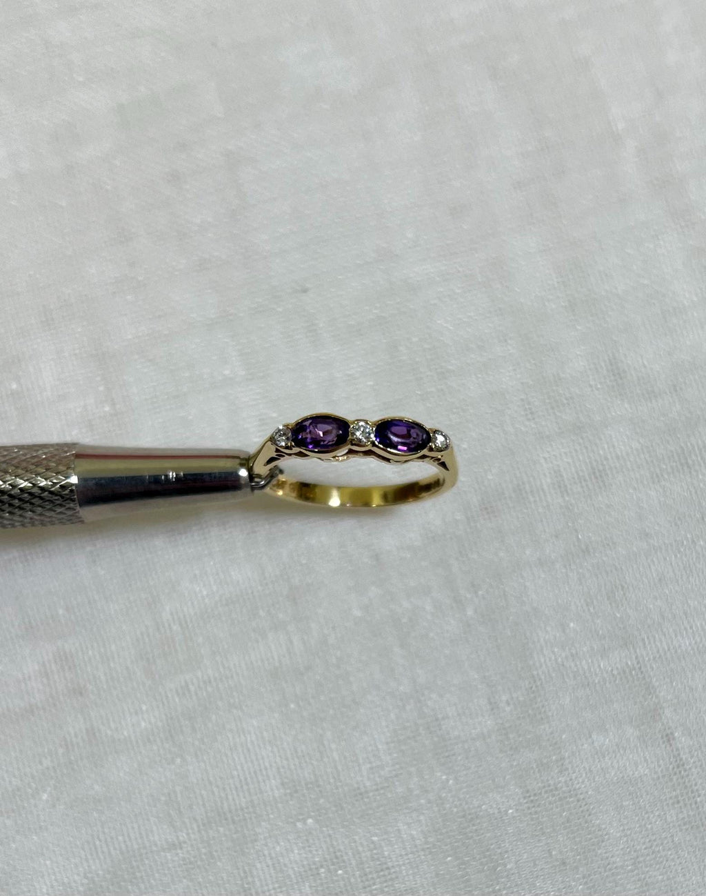 Gold ring with purple stones held by a tool on a white background