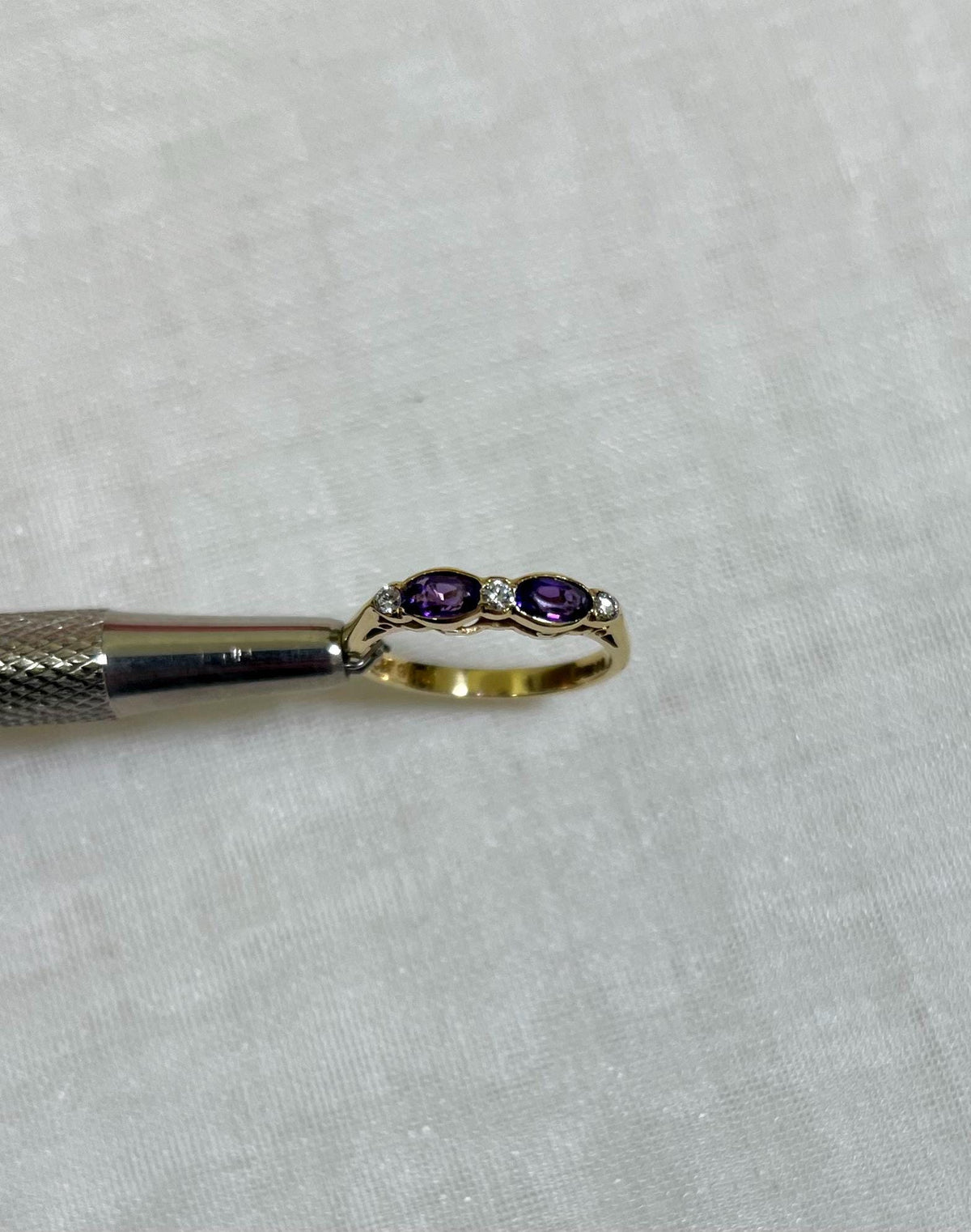 Gold ring with purple stones held by a tool on a white background