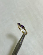 Gold ring with purple gemstone held by tweezers on a light beige background