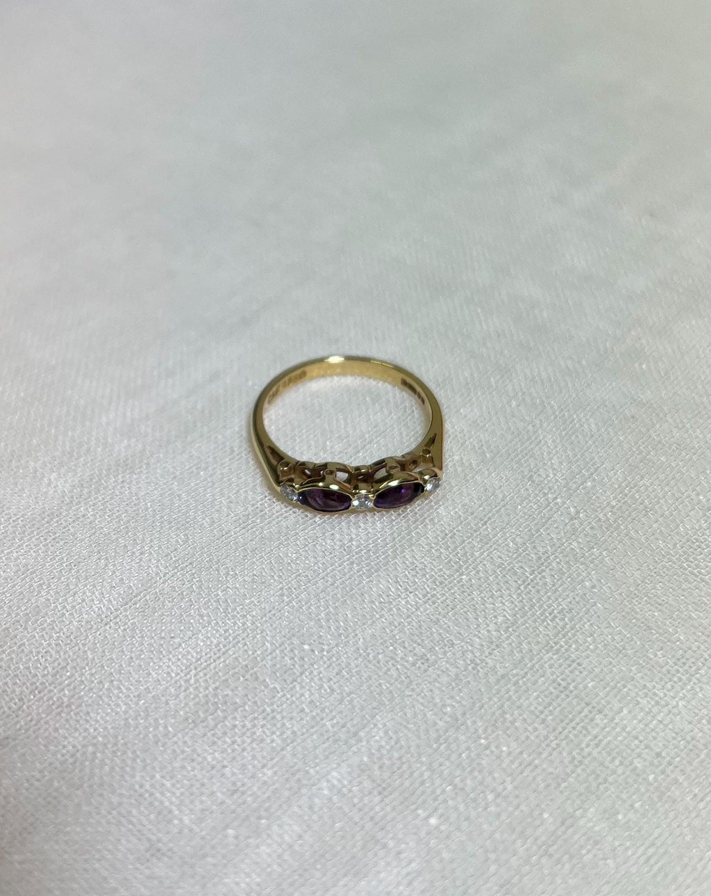 Gold ring with purple stones on a light beige background