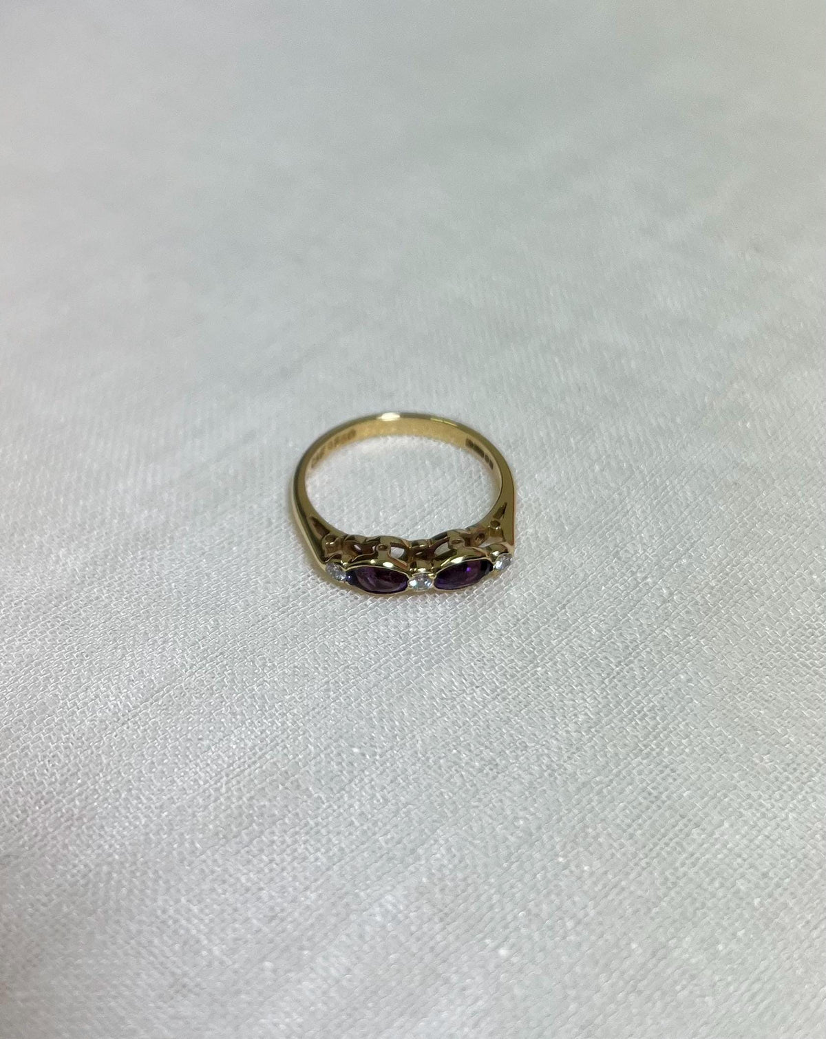 Gold ring with purple stones on a light beige background