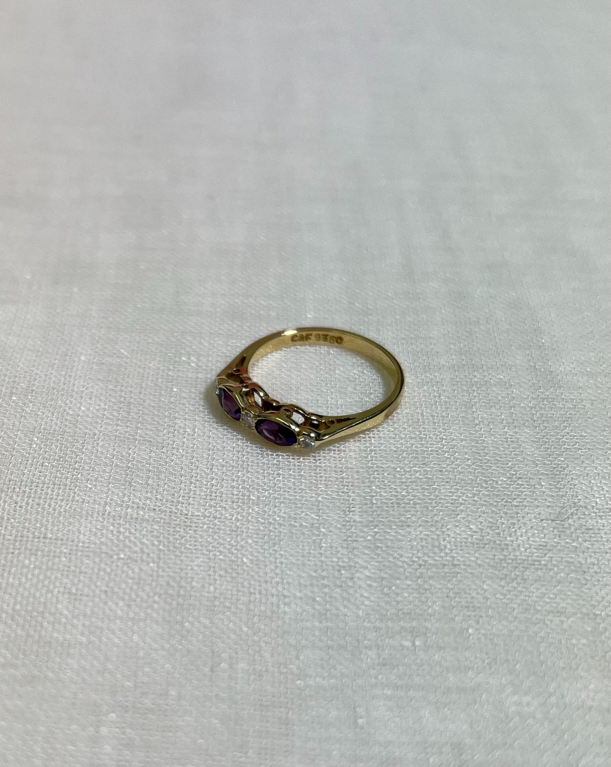 Gold ring with purple gemstones on a light beige fabric background
