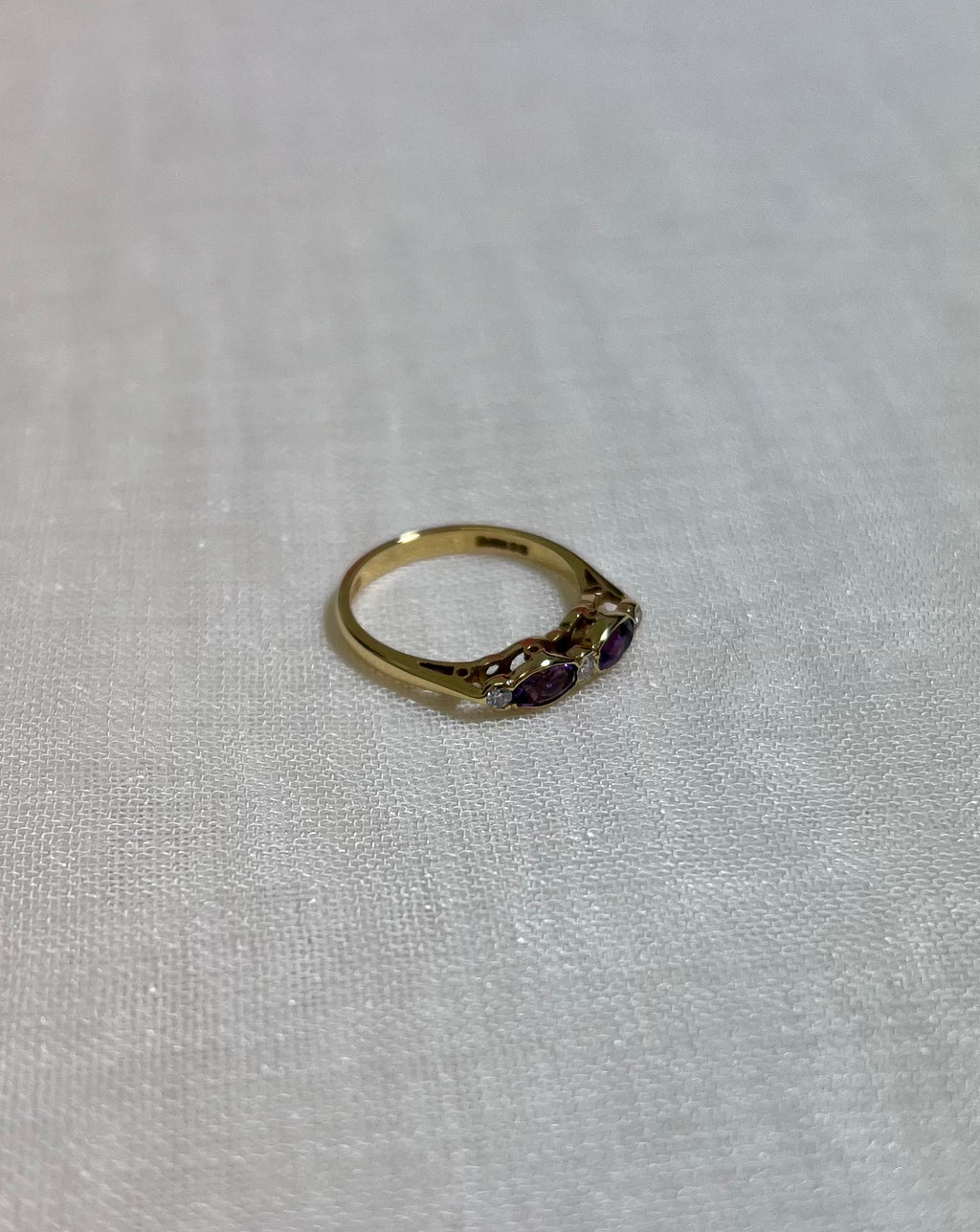 A gold ring with purple gemstones on cream fabric background