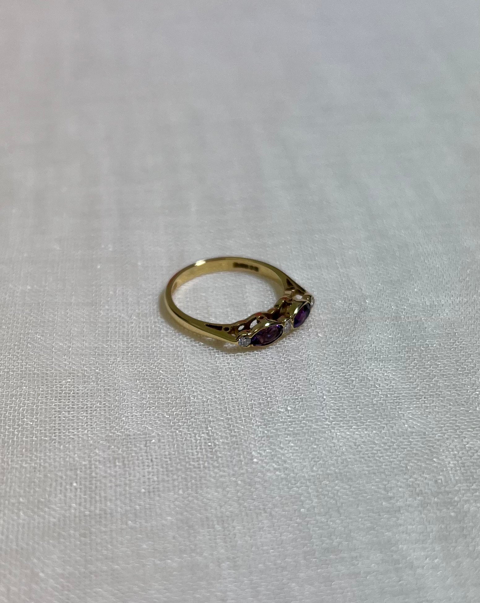 A gold ring with purple gemstones on cream fabric background