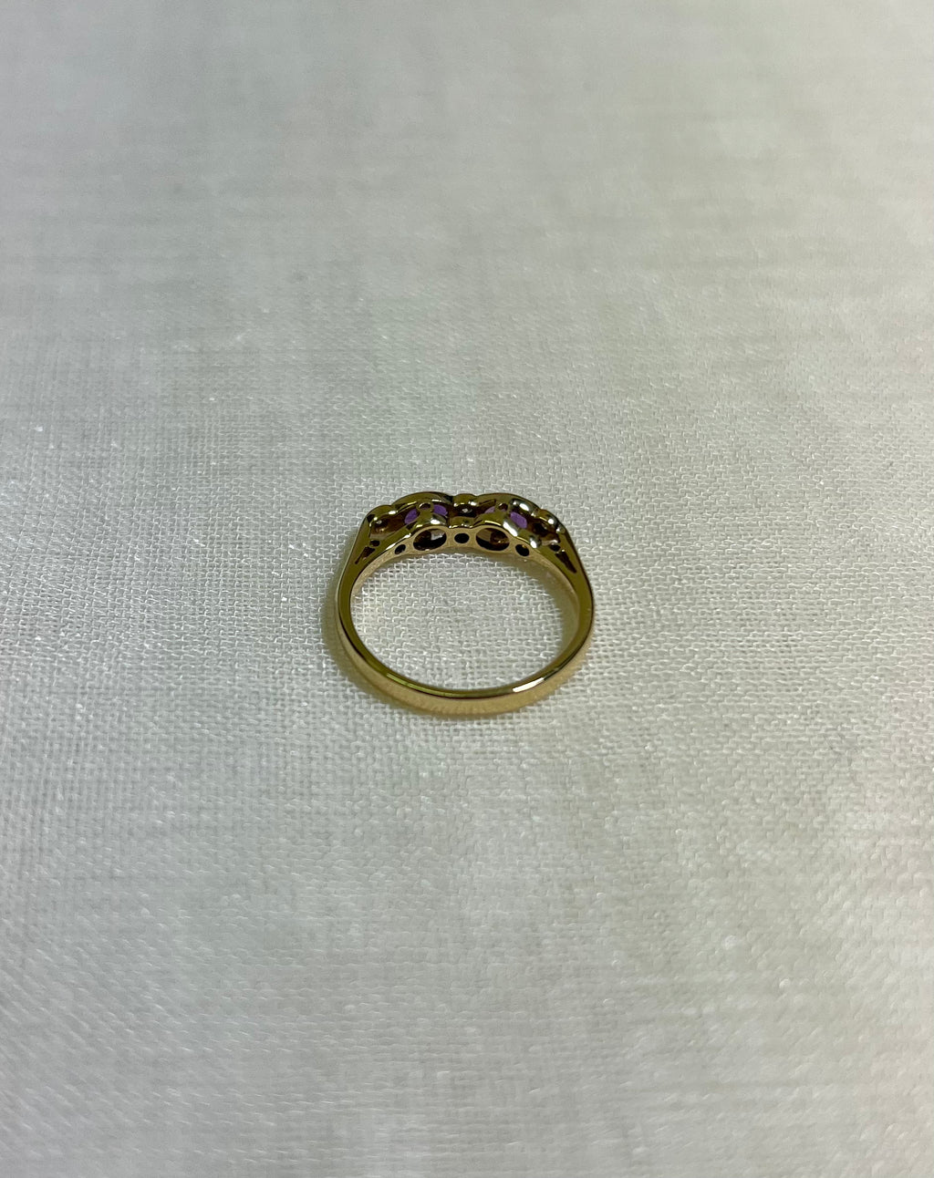 a gold ring with purple gemstones on light beige fabric background