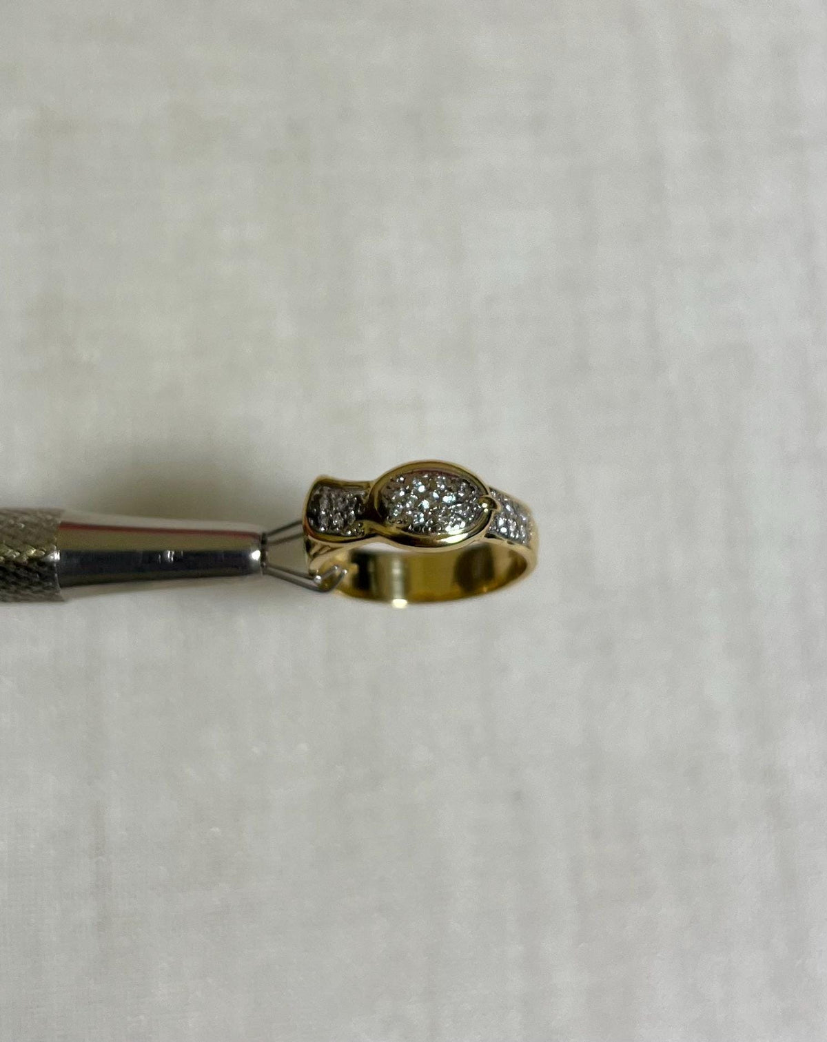 Gold ring with diamond accents held with silver tool above cream background 
