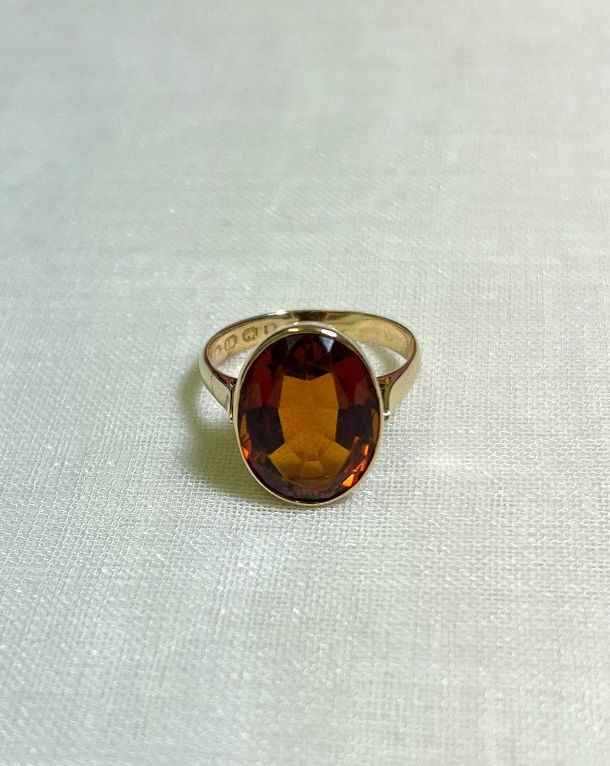 Gold Ring with oval citrine stone on white fabric background