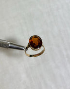 Gold ring with oval citrine stone held by silver tool against white fabric background 
