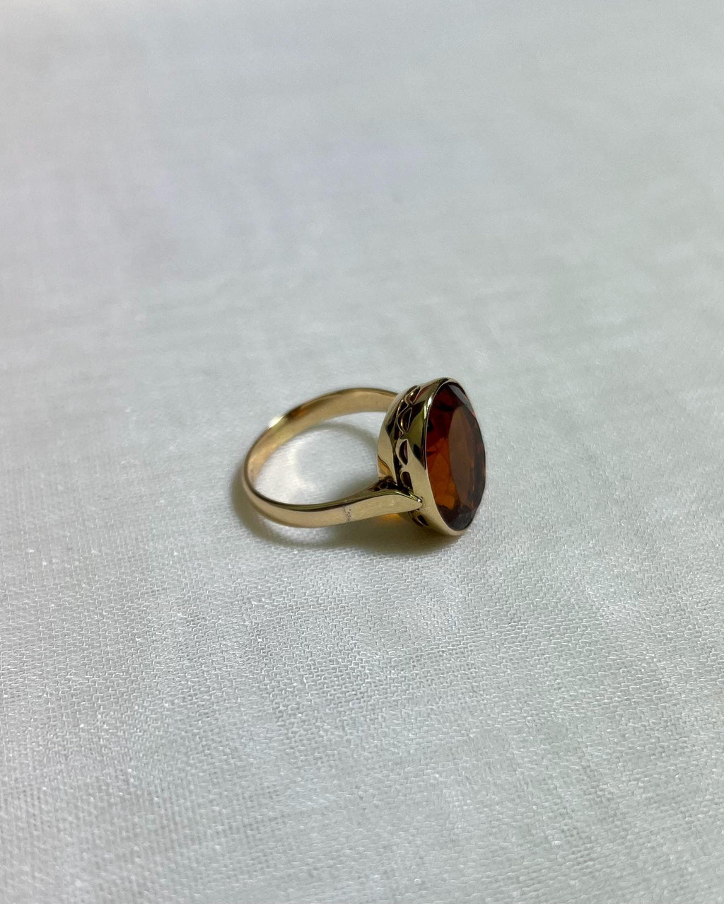 side view of Gold ring with orange stone on white fabric background