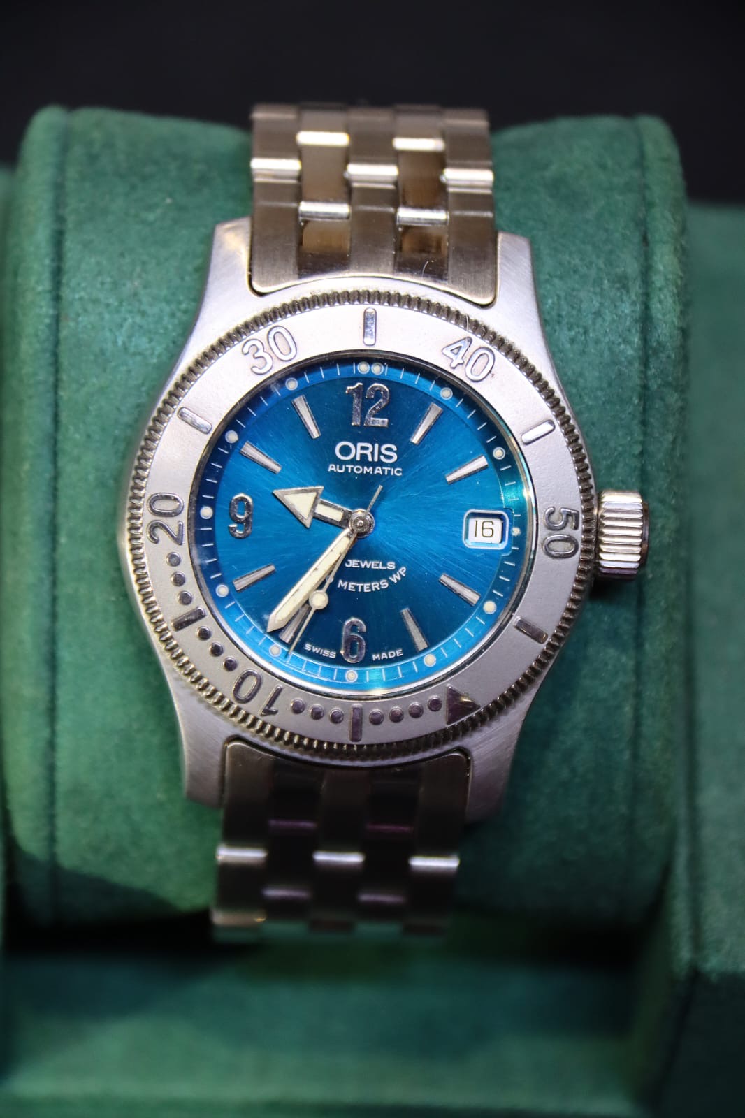 An Oris Big Crown Automatic watch with blue dial and brushed satin effect stainless steel case and bracelet, displayed on green cushion.
