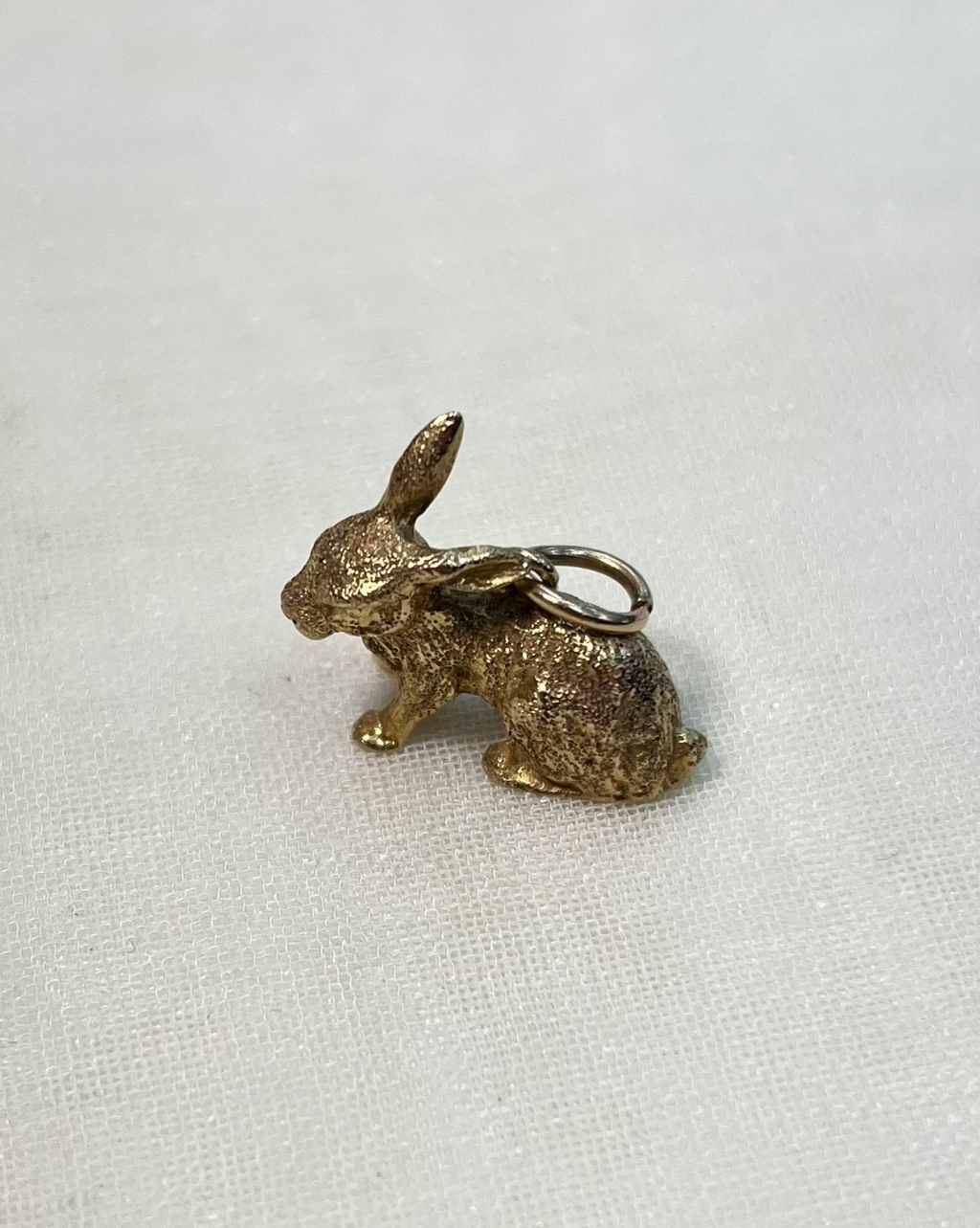 gold rabbit charm resting on white fabric background