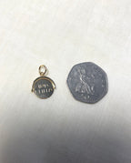 A small round gold pendant with happy birthday engraving, shown next to a silver 50 pence coin for scale on a light fabric background.