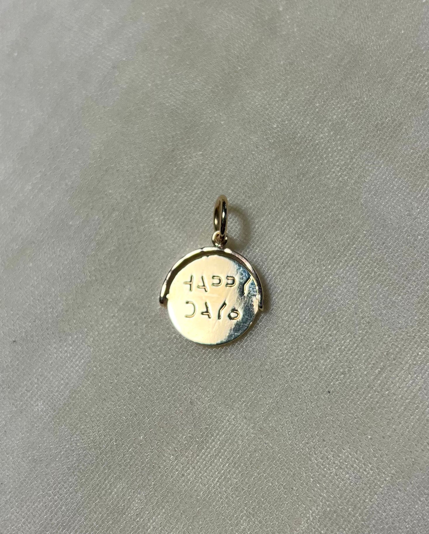 gold round pendant with ' happy days' message on cream linen background 