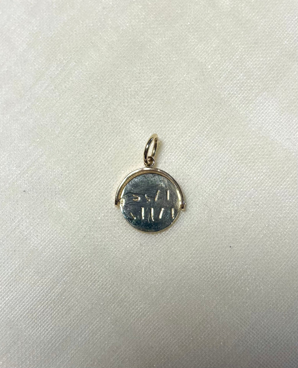gold round charm with engraving on cream linen background