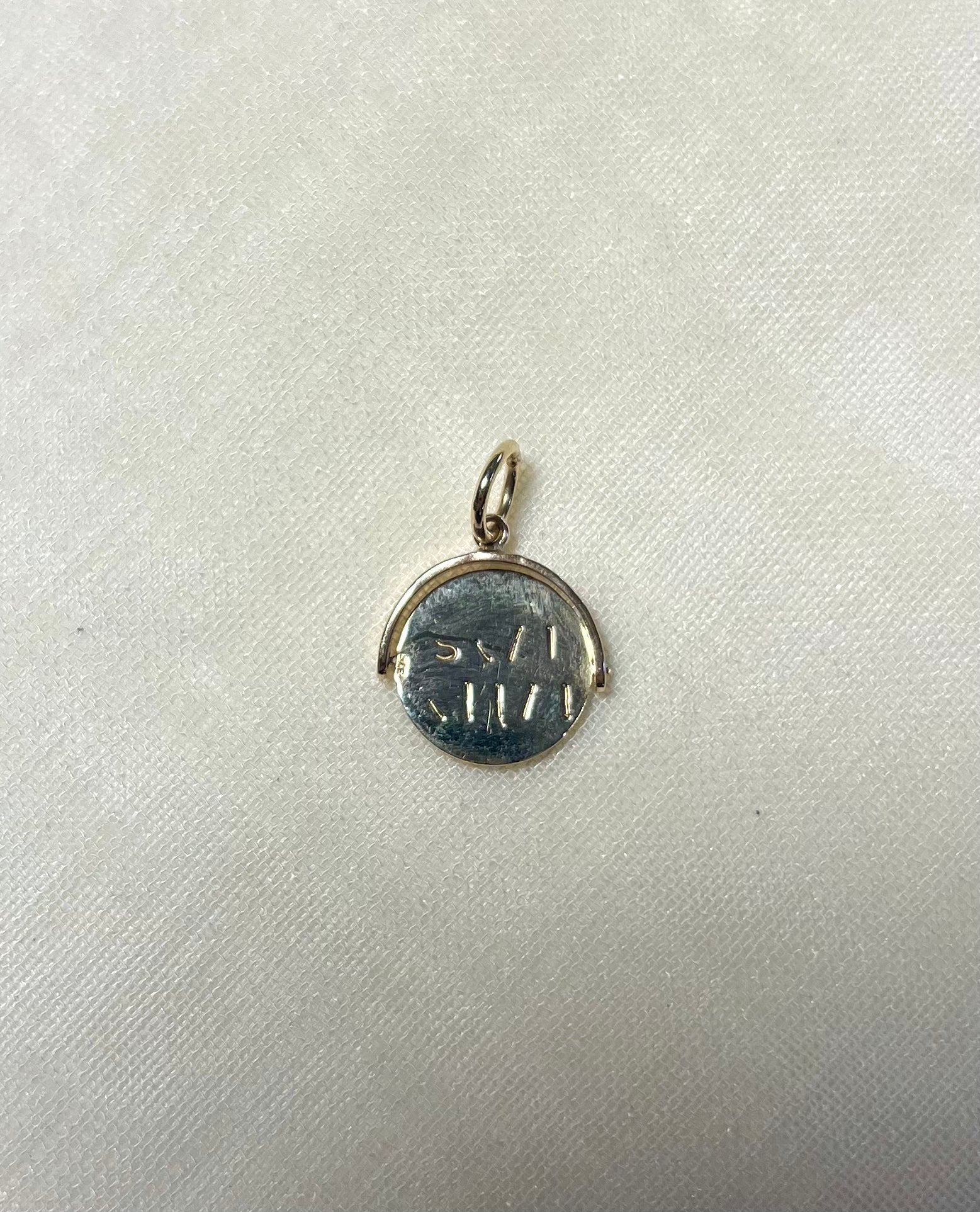 gold round charm with engraving on cream linen background
