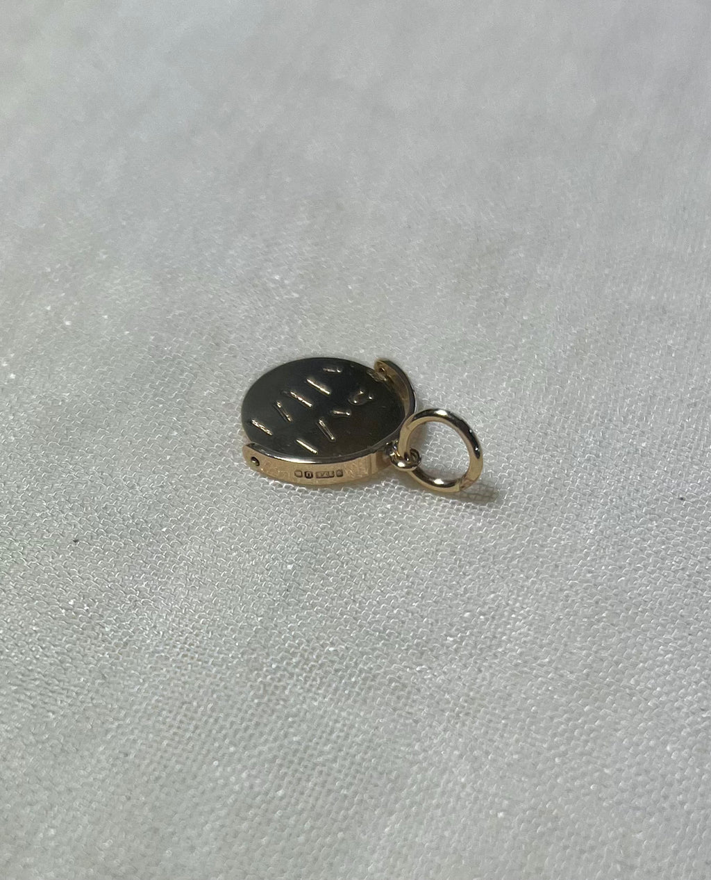 top view of gold round charm with visible hallmark, on cream linen background