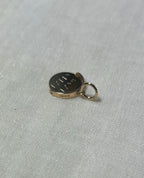 top view of gold round charm with visible hallmark, on cream linen background