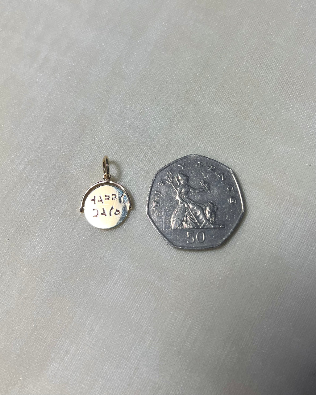 gold round charm next to 50p coin on cream linen background