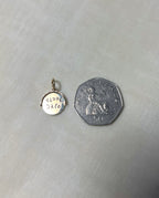 gold round charm next to 50p coin on cream linen background