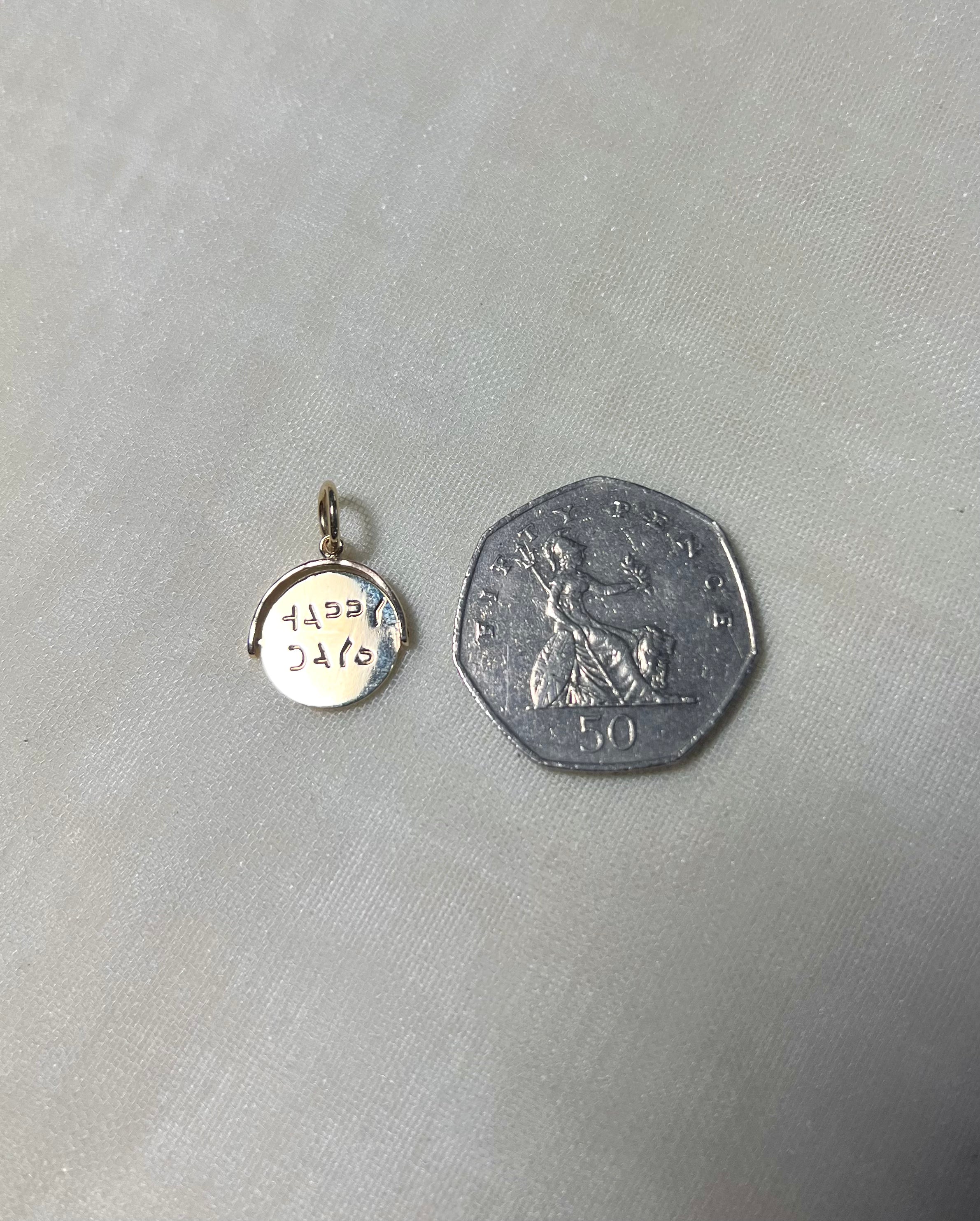 gold round charm next to 50p coin on cream linen background