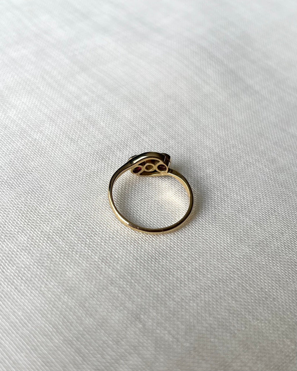 back view of gold ring set with three gemstones, resting on textured white linen fabric.