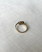 back view of gold ring set with three gemstones, resting on textured white linen fabric.
