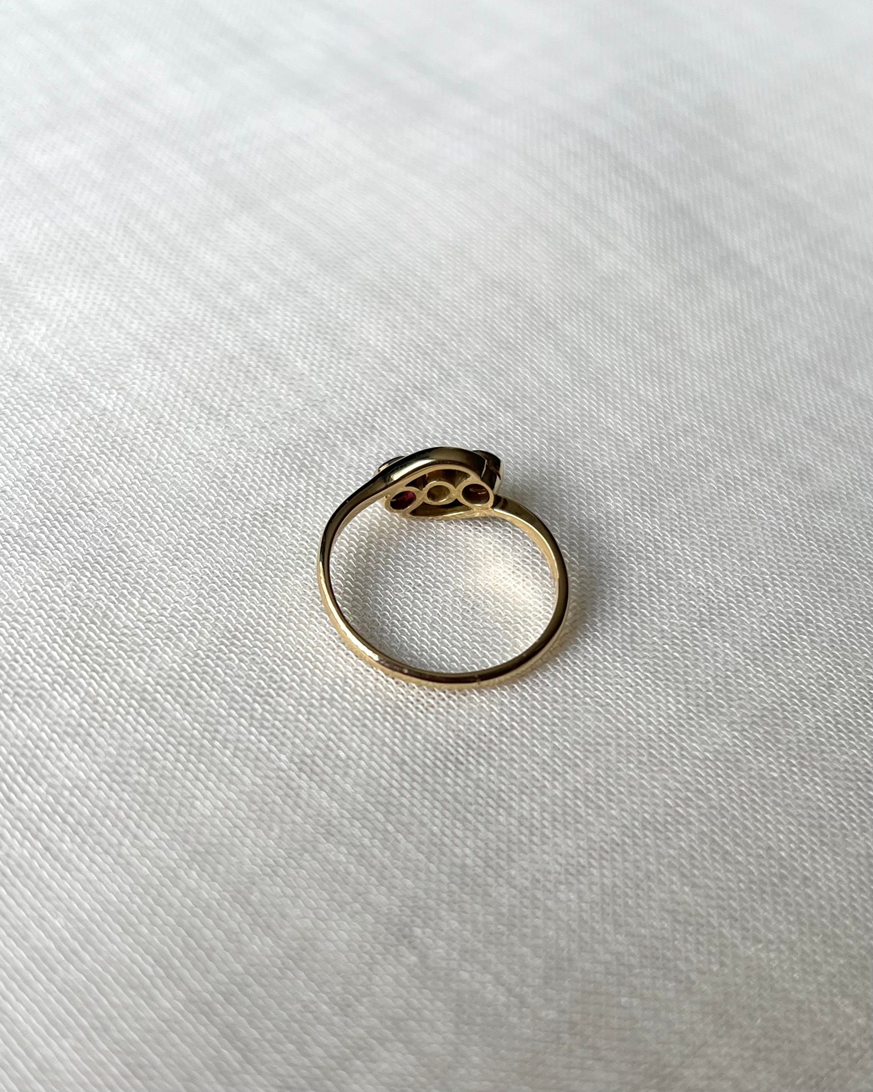 back view of gold ring set with three gemstones, resting on textured white linen fabric.