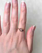 A gold ring with three small round gemstones of rubies and a diamond with crossover design, worn on a person's finger against a light neutral background.