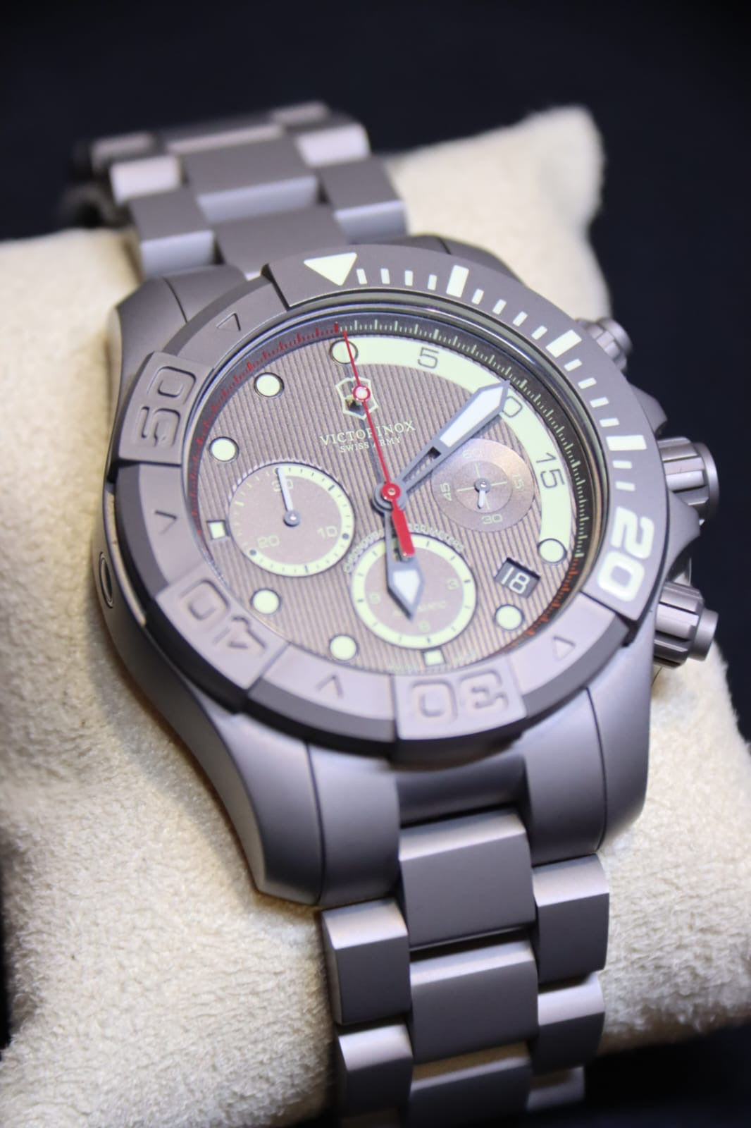A close-up of a Victorinox wristwatch with titanium case and bracelet, resting on a beige display cushion.
