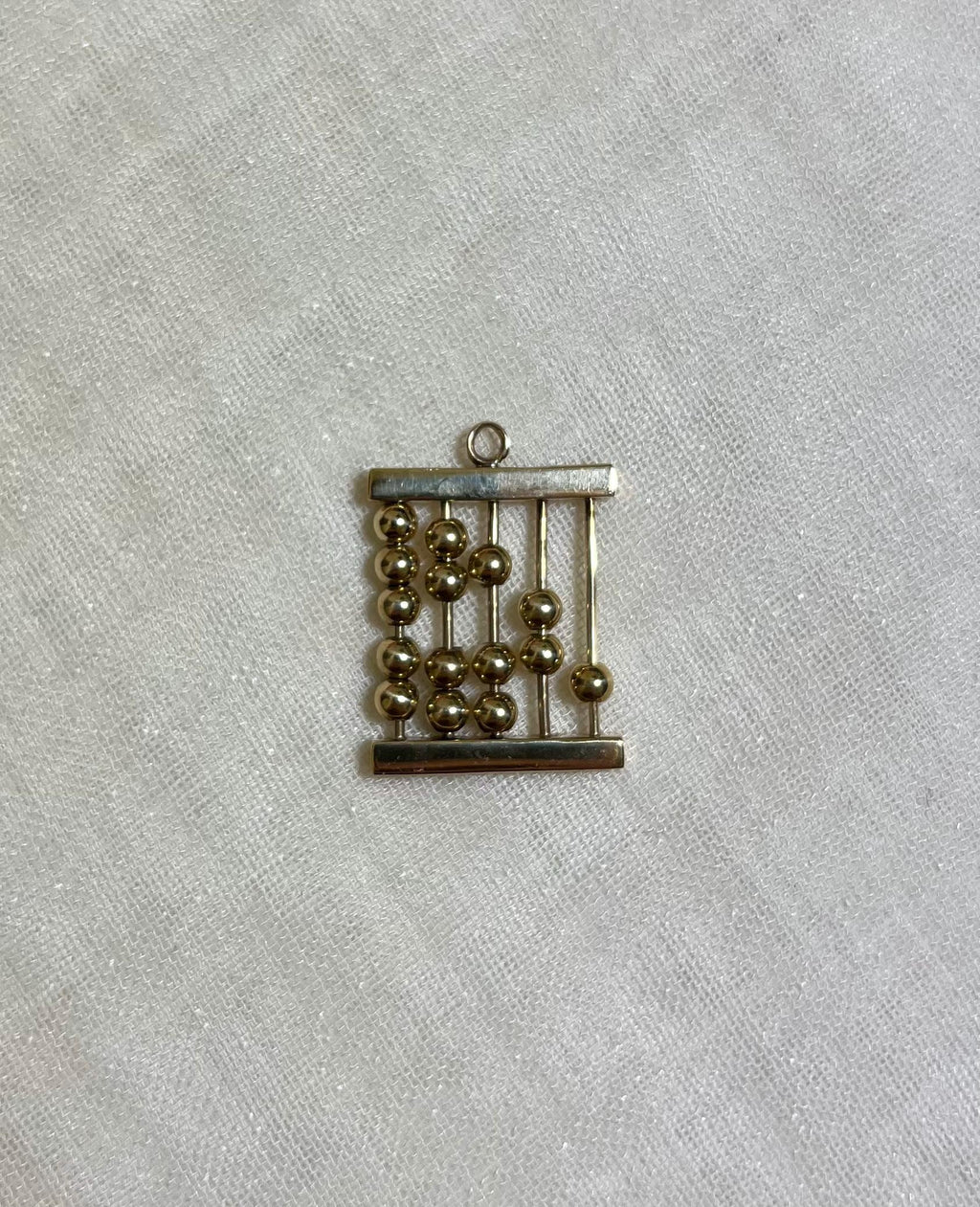 gold abacus charm on white fabric background 