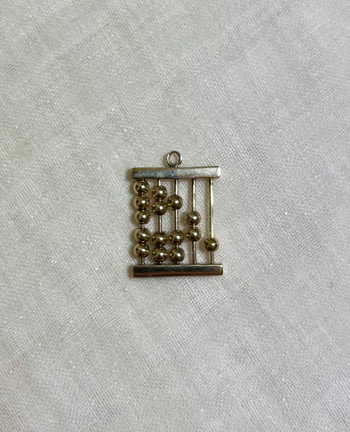gold abacus charm on white fabric background 