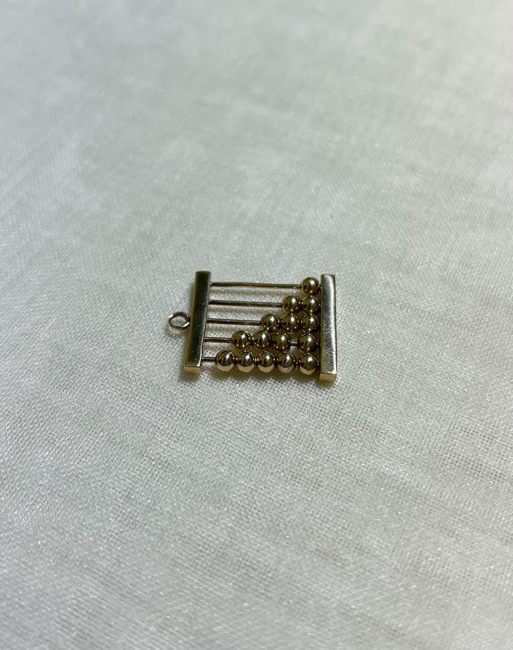 gold abacus charm on white fabric background