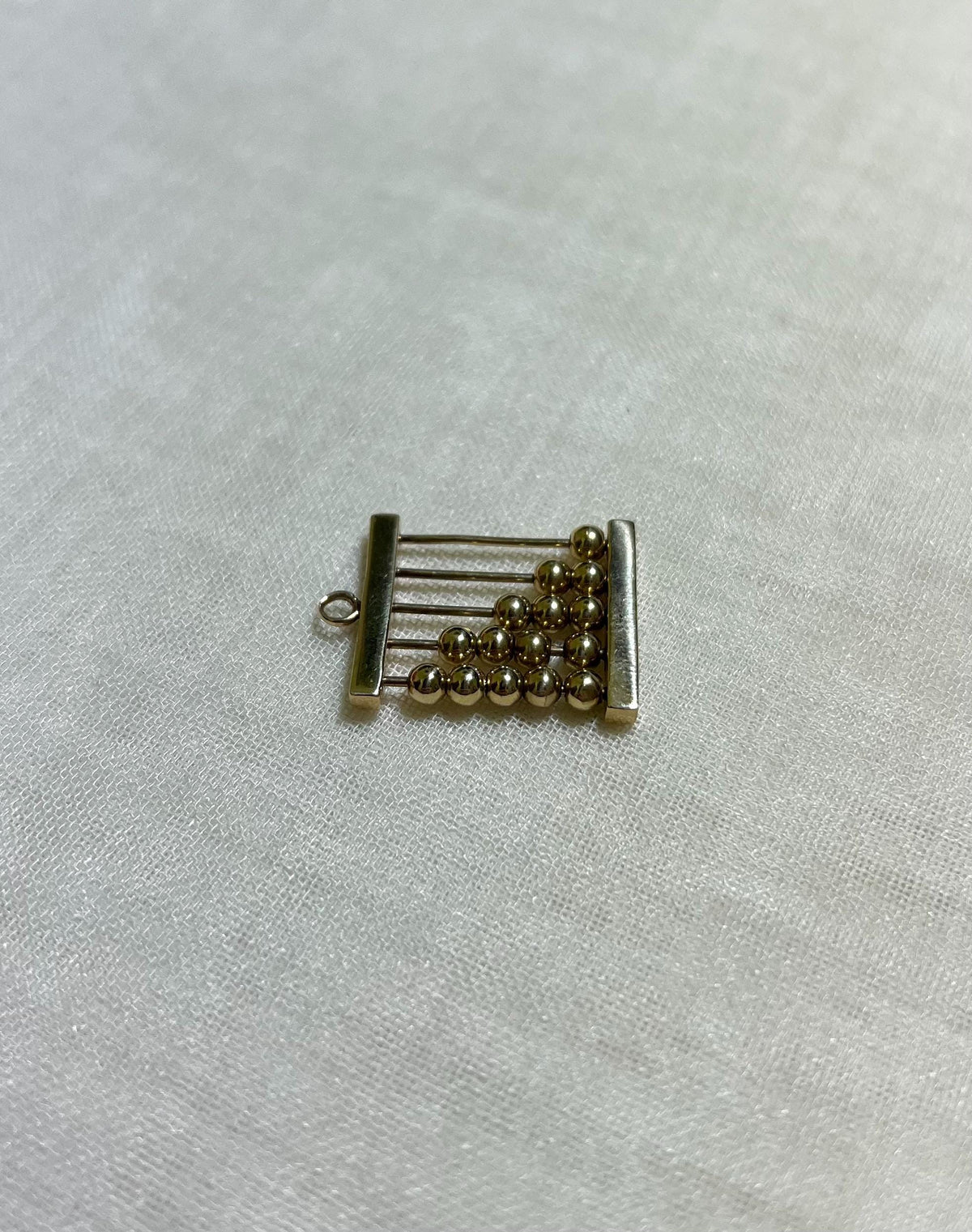 gold abacus charm on white fabric background