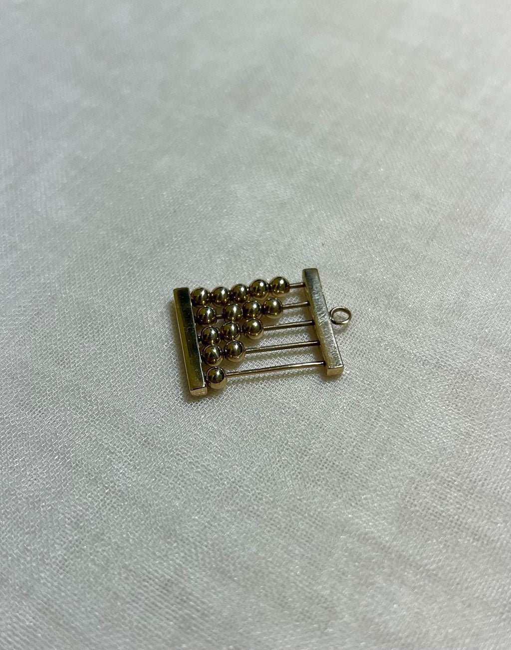 gold abacus charm on white fabric background 