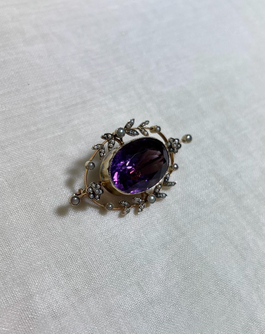 vintage brooch with large purple amethyst gemstone centre and pearl set accent on white fabric background