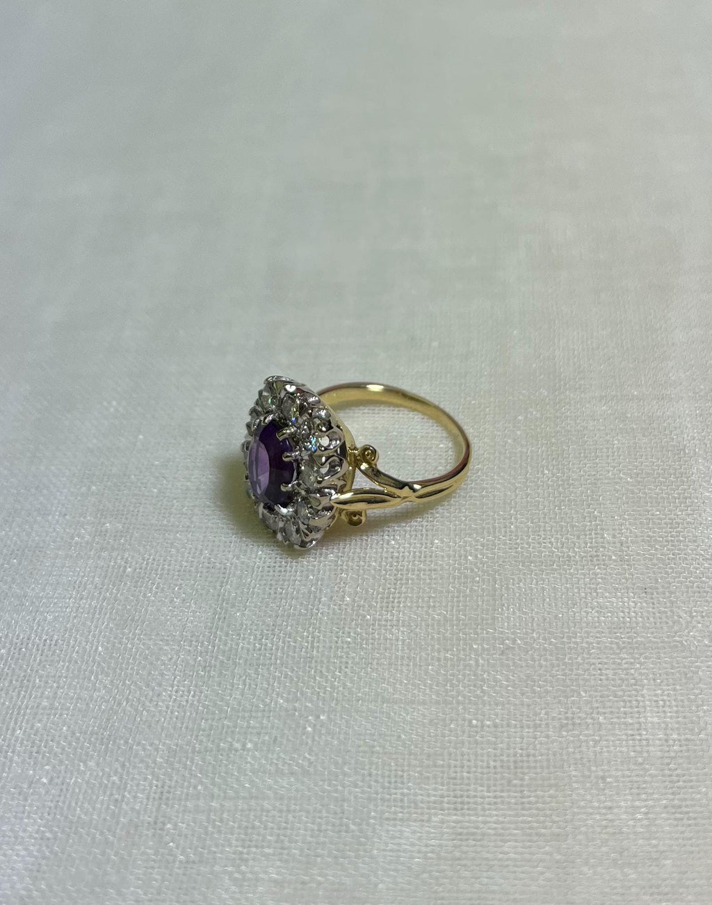 Gold ring with a purple gemstone and diamond accents on a white fabric background