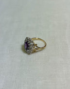 Gold ring with a purple gemstone and diamond accents on a white fabric background