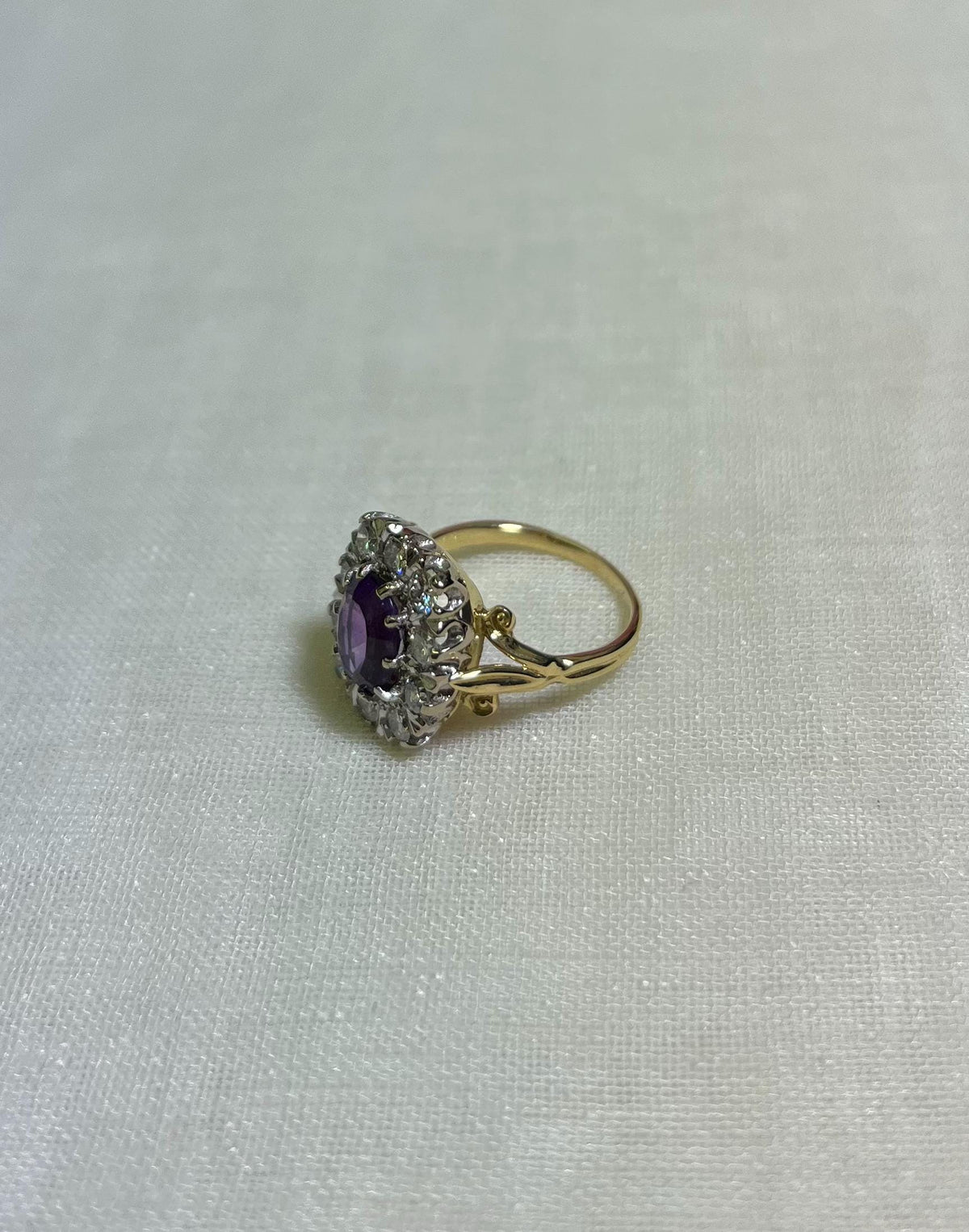 Gold ring with a purple gemstone and diamond accents on a white fabric background