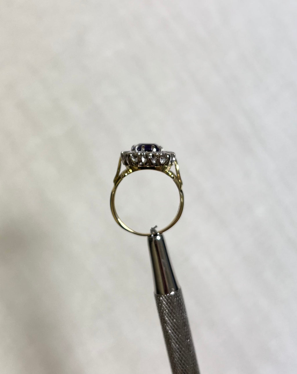 side view of gold ring held by silver tool above white background