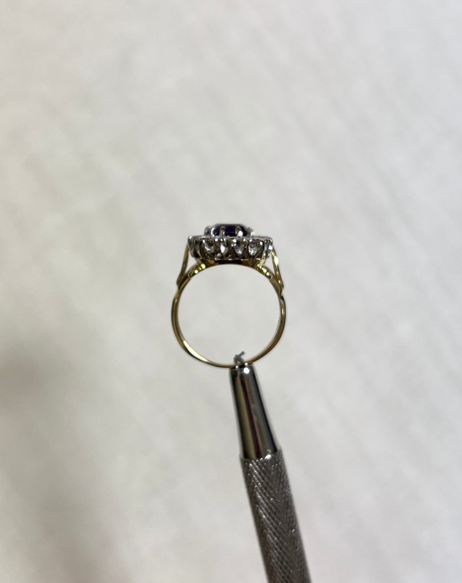 side view of gold ring held by silver tool above white background