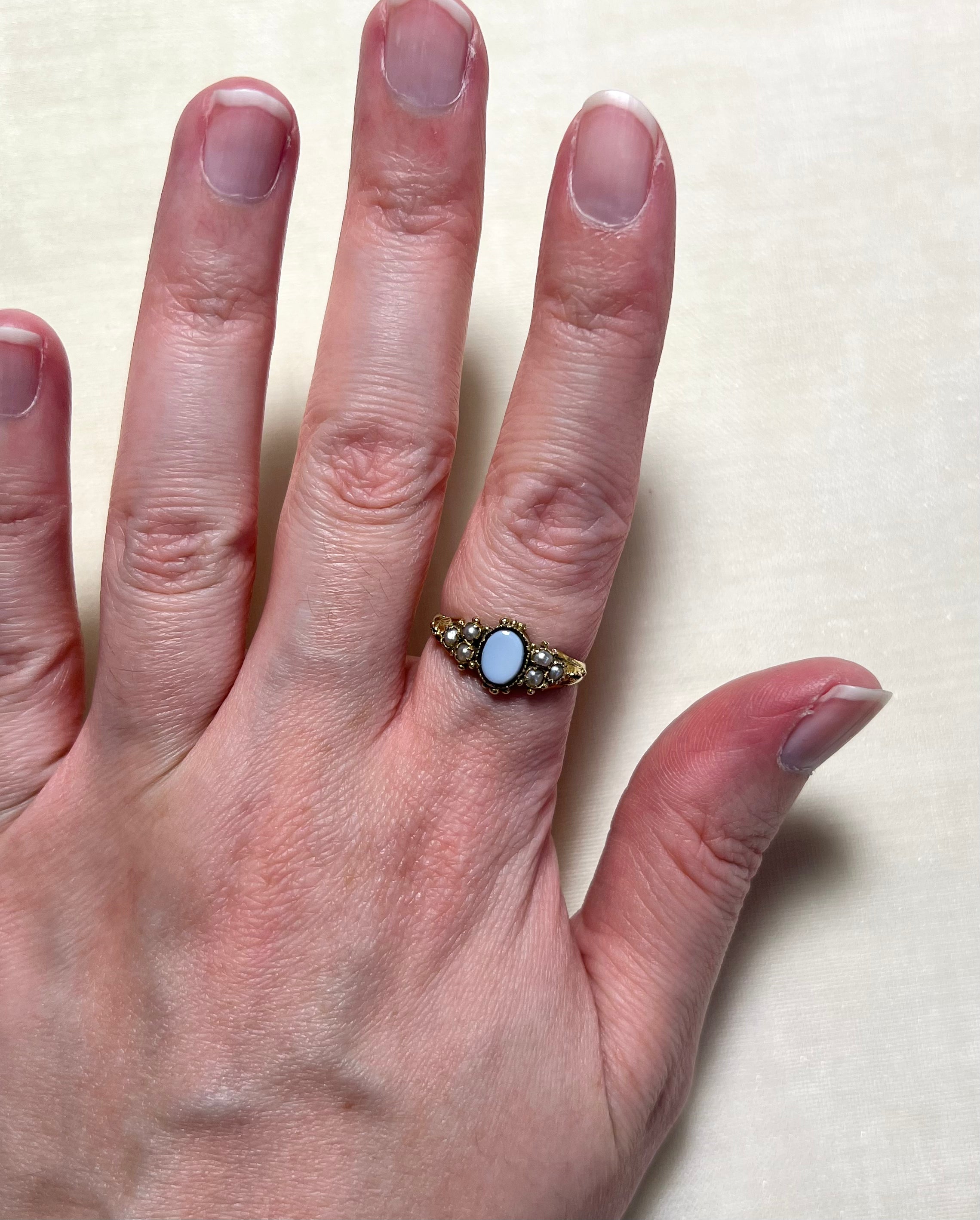 An antique gold ring with oval sardonyx and seed pearl, worn on hand against cream coloured background