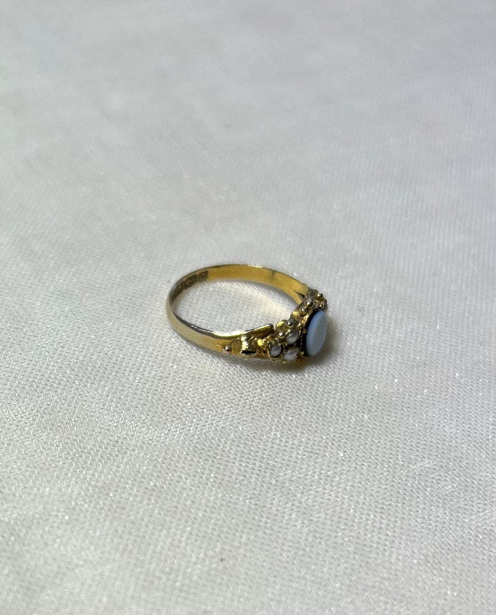 a gold ring with pearl and light blue cabochon, resting on cream linen background