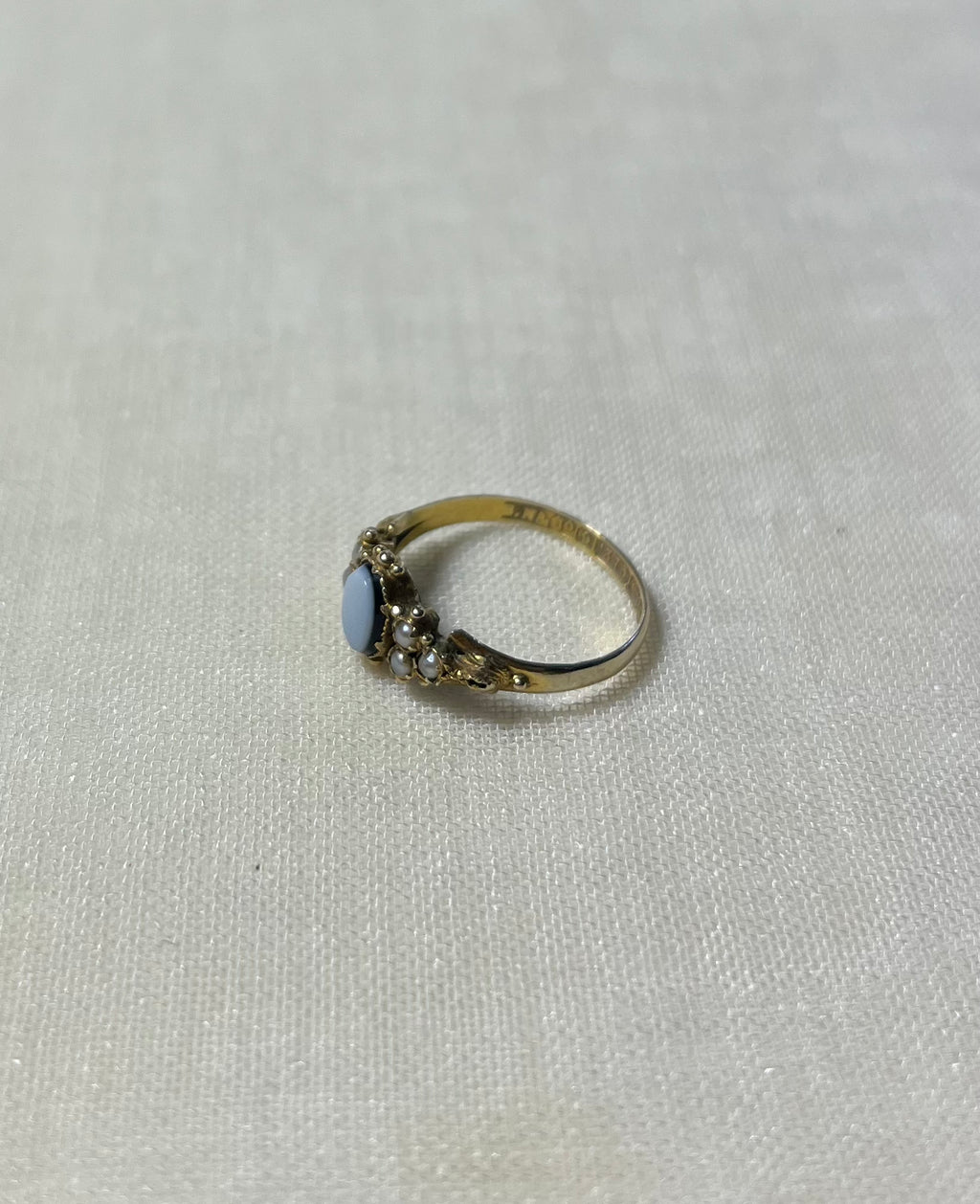 a gold ring with seed pearl and light blue stone, resting on cream linen background 