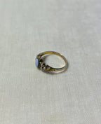a gold ring with seed pearl and light blue stone, resting on cream linen background 