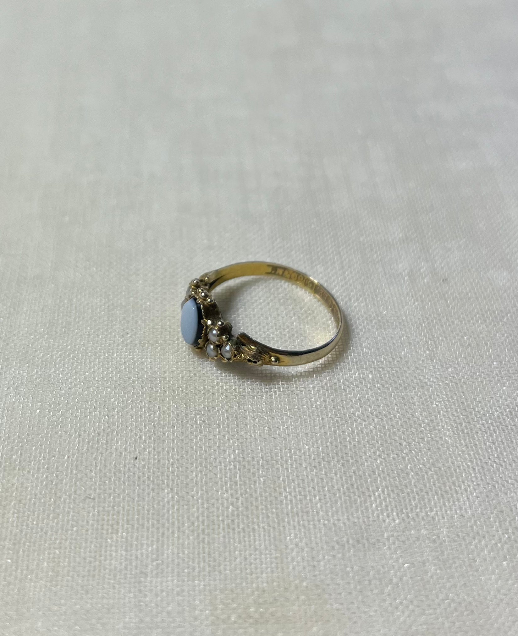 a gold ring with seed pearl and light blue stone, resting on cream linen background 
