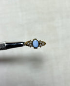 an antique gold ring set with seed pearl and an oval sardonyx stone in the centre, held by silver tool above cream coloured background 