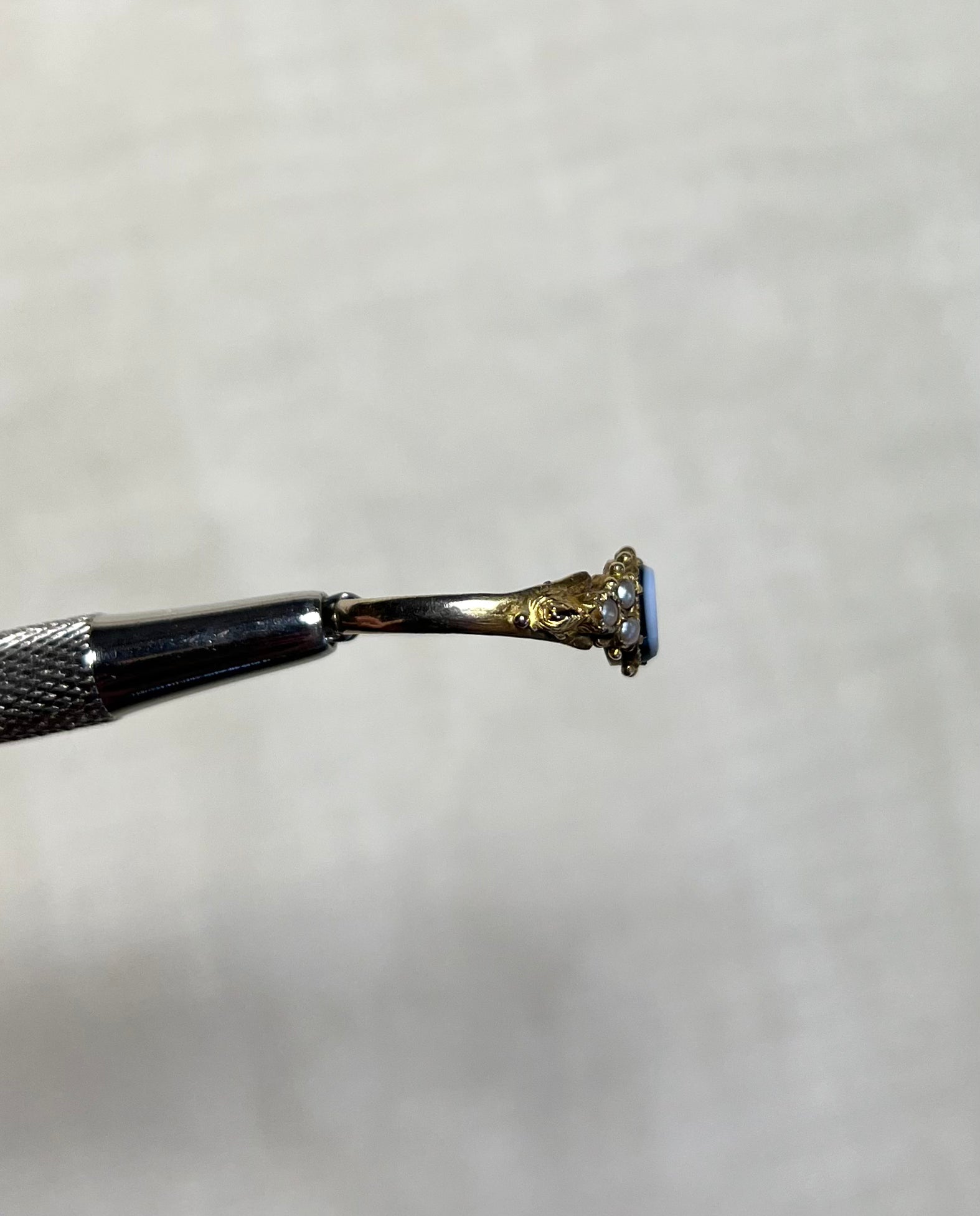 side view of gold ring head by silver tool above cream coloured background
